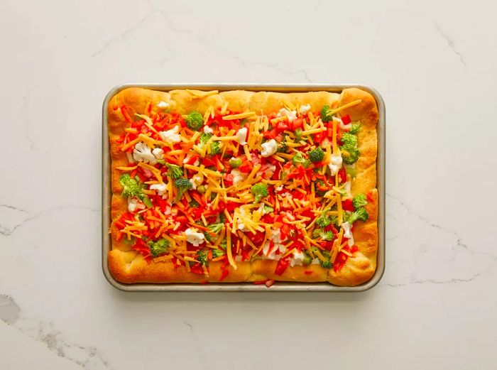 Overhead shot of a fully prepared vegetable pizza on a baking dish