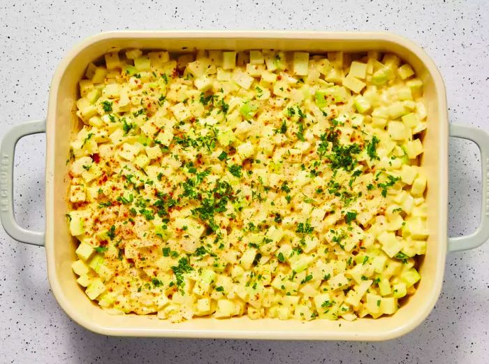 A greased baking dish filled with the zucchini-onion mixture, topped with parsley and a dusting of paprika.