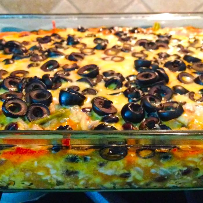 A close-up view of a vibrant Enchilada Casserole, topped with black olives, inside a glass baking dish.