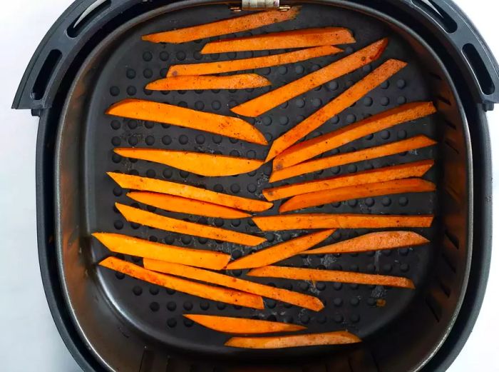 A top-down view of sliced and seasoned sweet potatoes arranged in a single layer in the air fryer.