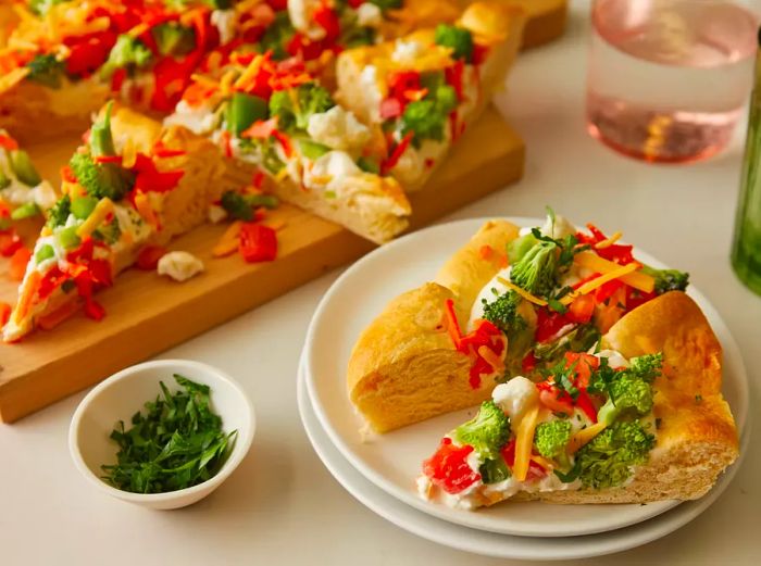 View of two slices of vegetable pizza on a plate, with the rest remaining on the cutting board