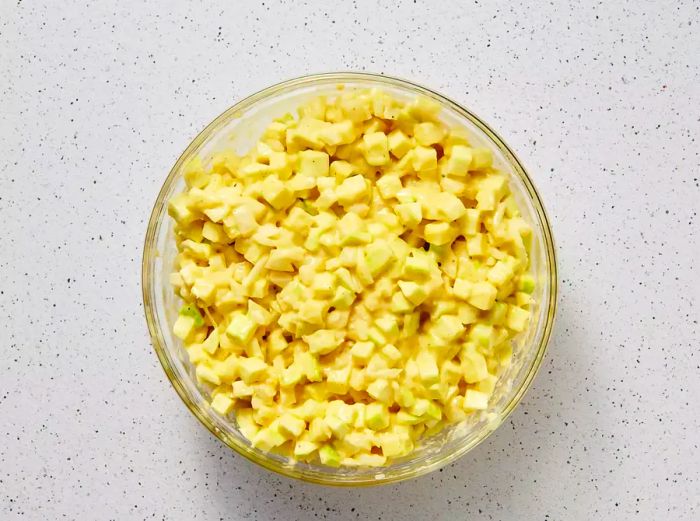 A large mixing bowl filled with chopped zucchini and onions, coated with a mixture of eggs, flour, and baking soda.