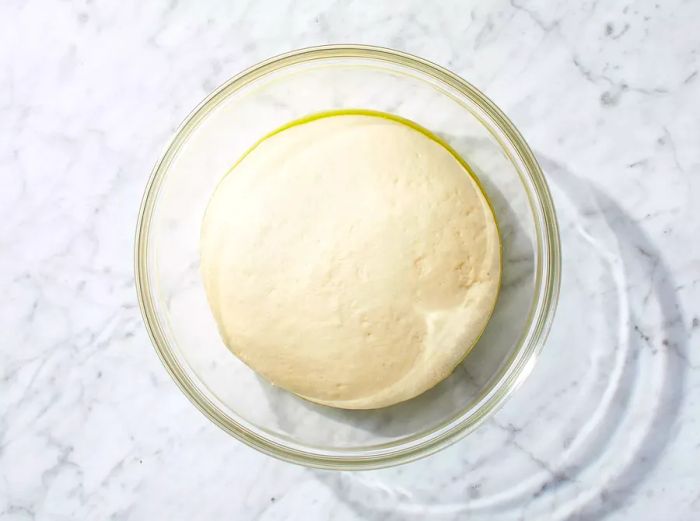 Dough placed in an oiled bowl, left to rise until it doubles in size.