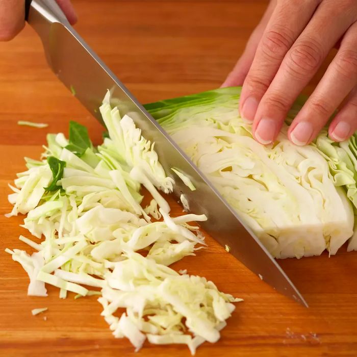 A person slicing a cabbage wedge into delicate, thin strips