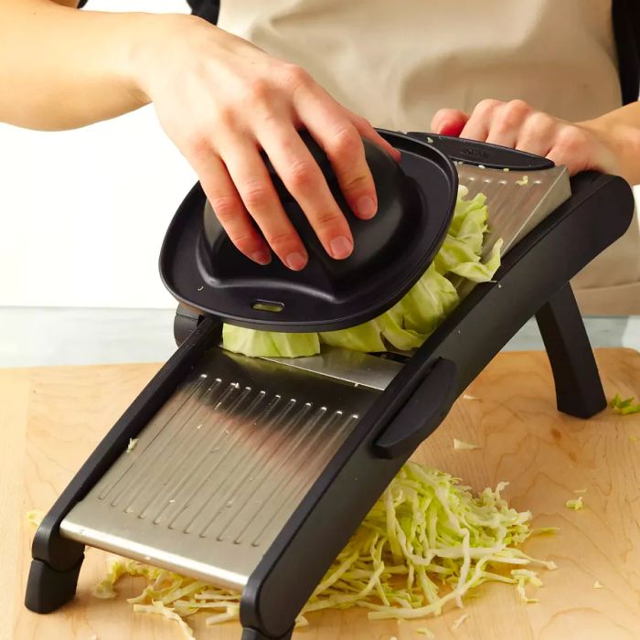 A person slicing cabbage on a mandoline using the safety guard