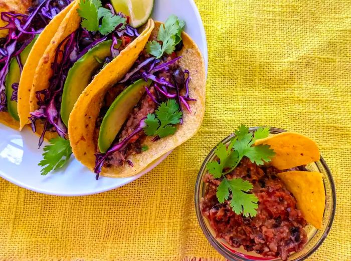 Vegan bean taco filling served in a bowl with chips for dipping and on a platter of tacos.