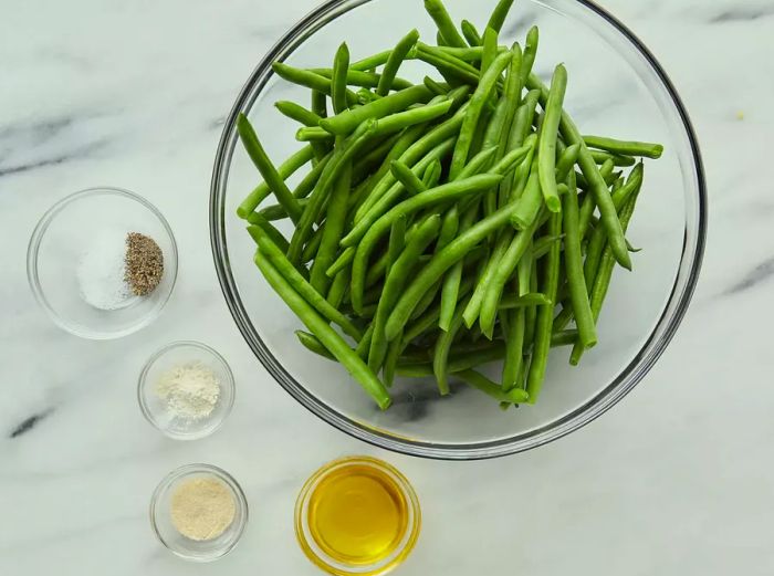 An overhead shot of the ingredients for sautéed green beans neatly arranged in small bowls on a kitchen counter.