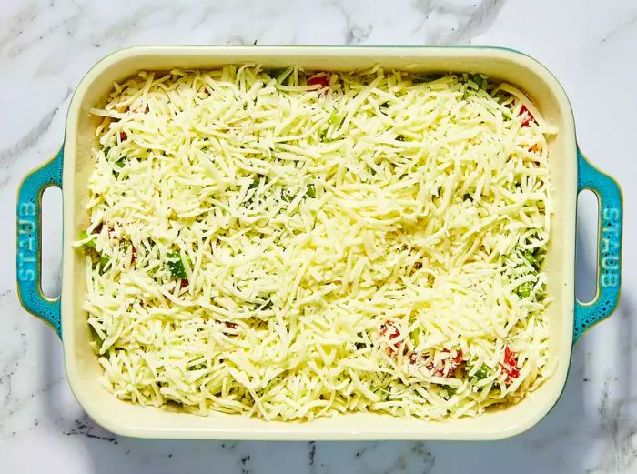 A baking dish filled with zucchini, onions, tomatoes, peppers, and Italian herbs, all topped with melted shredded cheese.