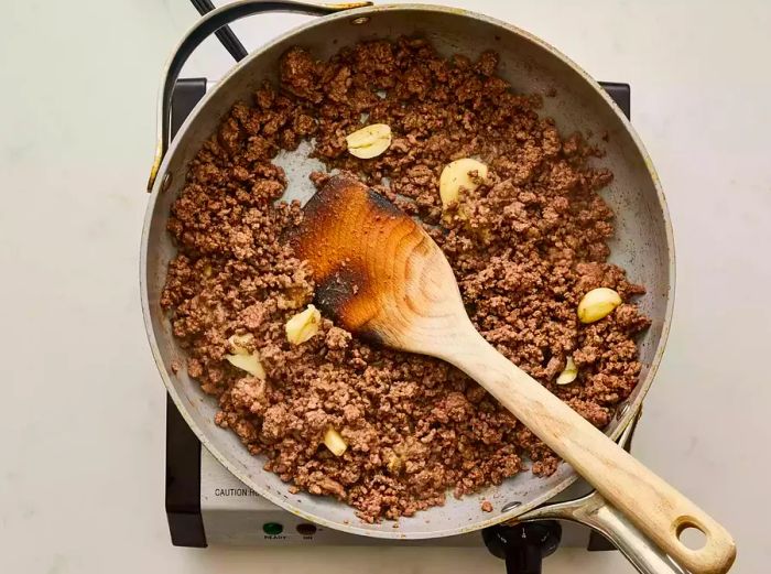 A skillet with cooked ground beef, garlic, ginger, and sesame oil