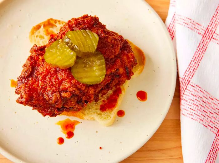 Overhead shot of Nashville hot chicken with pickle slices on top, served on bread and plated.