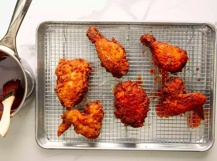 Aerial view of fried chicken on a baking sheet rack with sauce on the side