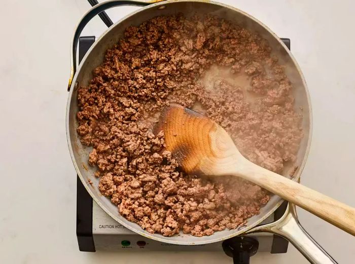 A large skillet with cooked ground beef inside