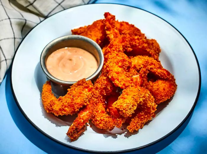 A plate of golden, crispy Japanese-style fried shrimp, accompanied by a small bowl of dipping sauce.