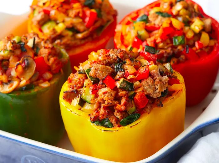 Close-up shot of red, orange, green, and yellow stuffed bell peppers filled with turkey and vegetables, placed in a baking dish.