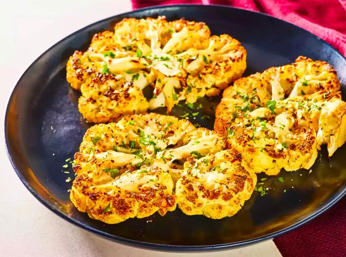 Three cauliflower steaks elegantly plated on a dark dish