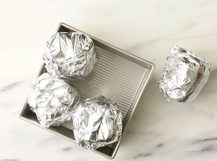 A high-angle view of the peppers wrapped in foil, resting in a baking dish.