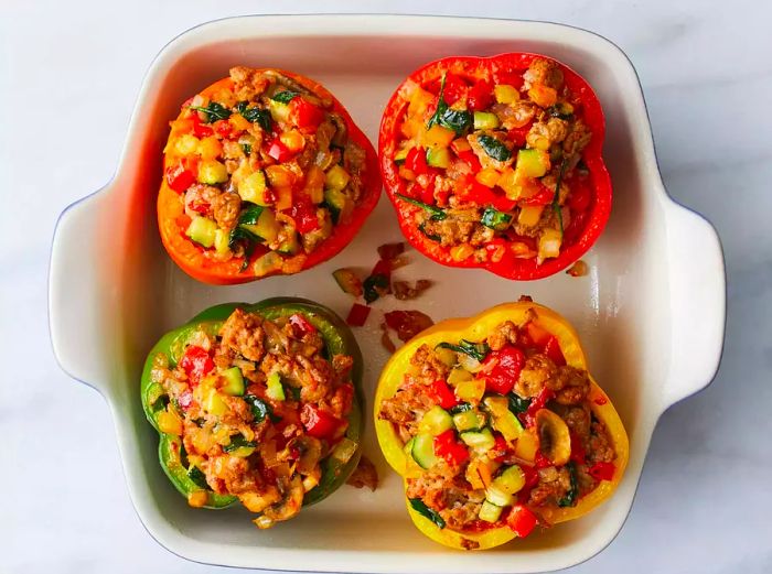 A top-down view of colorful stuffed peppers filled with turkey and vegetables, arranged in a baking dish.