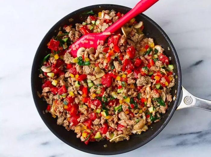 A top-down view of a skillet cooking the turkey and vegetable filling for stuffed peppers.