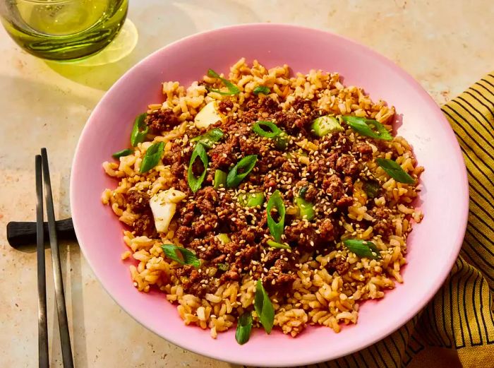 A Korean-style ground beef bowl served with brown rice, garnished with sesame seeds and sliced scallions