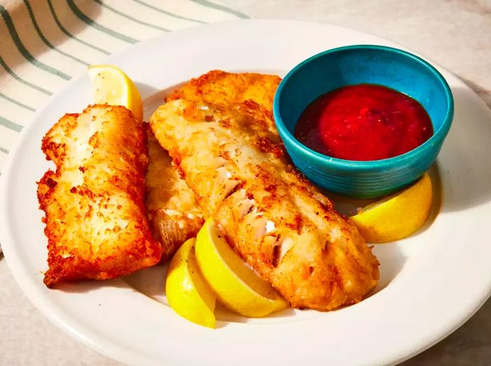 A plate of crispy beer-battered fried fish, accompanied by dipping sauce and lemon wedges