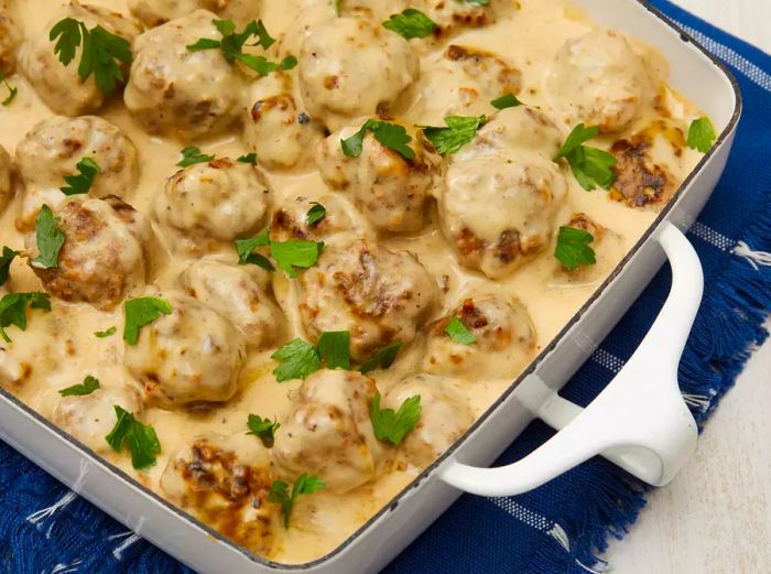 High-angle shot of the completed Swedish Meatballs (Svenska Köttbullar) served in a dish, garnished with fresh herbs.