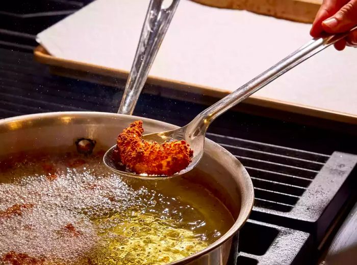 A slotted spoon lifting a crispy shrimp from a pot of bubbling hot oil.