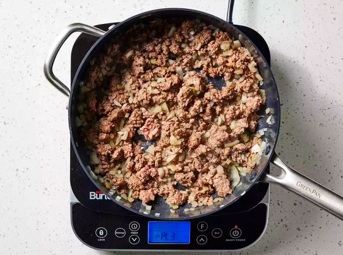 A skillet filled with browned ground beef, chopped onions, and fragrant basil.