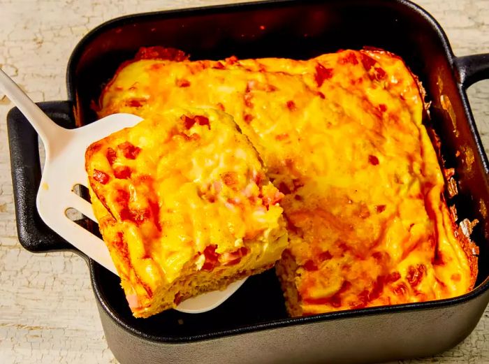 An overhead shot of a slice of baked omelet being lifted from a dark baking dish.