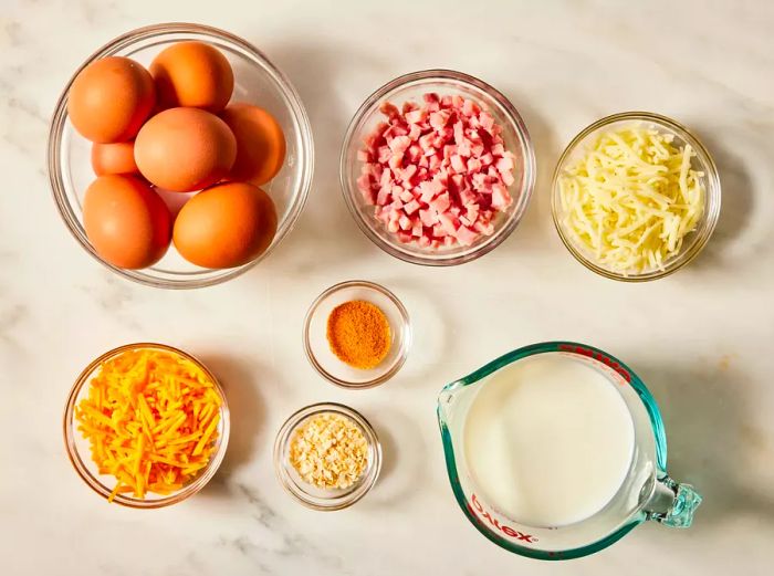 An overhead shot showcasing all the ingredients for the baked omelet neatly arranged in small glass bowls.