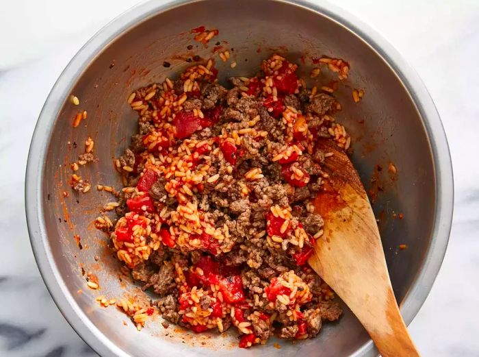 Aerial shot of a bowl with rice, tomatoes, and ground beef being mixed together for stuffed peppers.