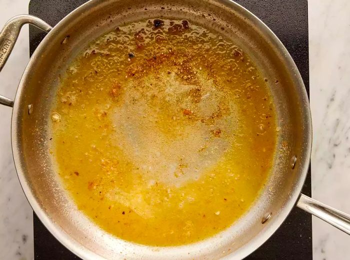 Overhead view of a pan with lemon sauce simmering and reducing