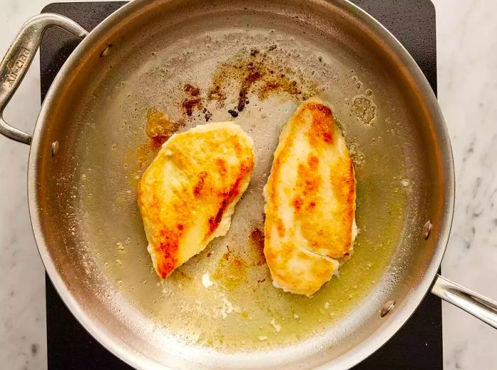 Overhead view of two chicken breasts being seared in a pan