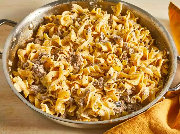 A close-up shot of beef stroganoff cooking in a pan, next to a kitchen towel.