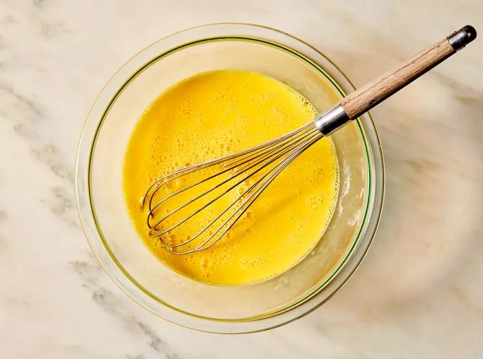 An overhead view of eggs being whisked in a glass mixing bowl.