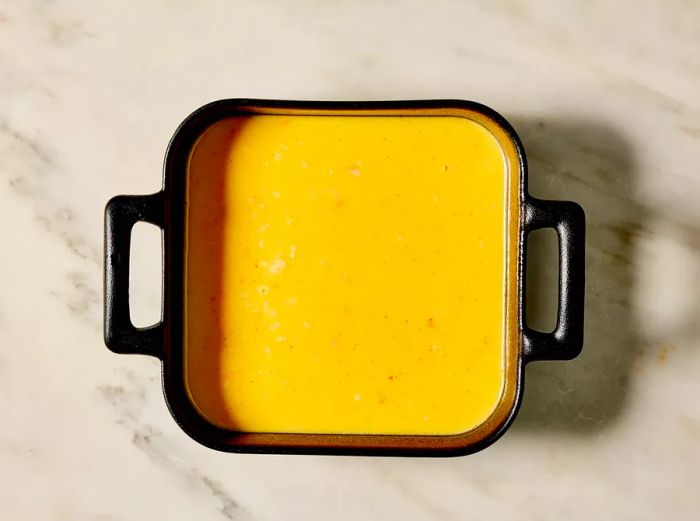 An overhead view of the prepared egg mixture being poured into a dark, square baking dish.