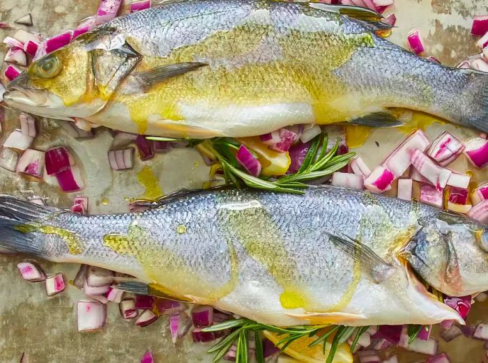 An overhead view of two whole branzino fish drizzled with olive oil.