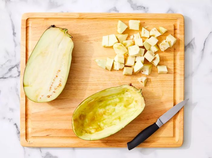 An eggplant split in half with the flesh scooped out, leaving a 1/2-inch thick shell, and the reserved flesh being cut into 1/2-inch cubes.