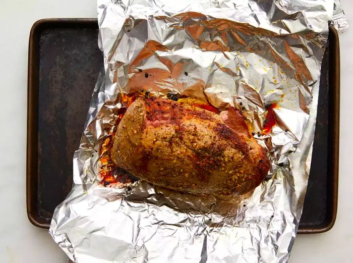 Partially cooked beef roast resting on tinfoil on a baking sheet.