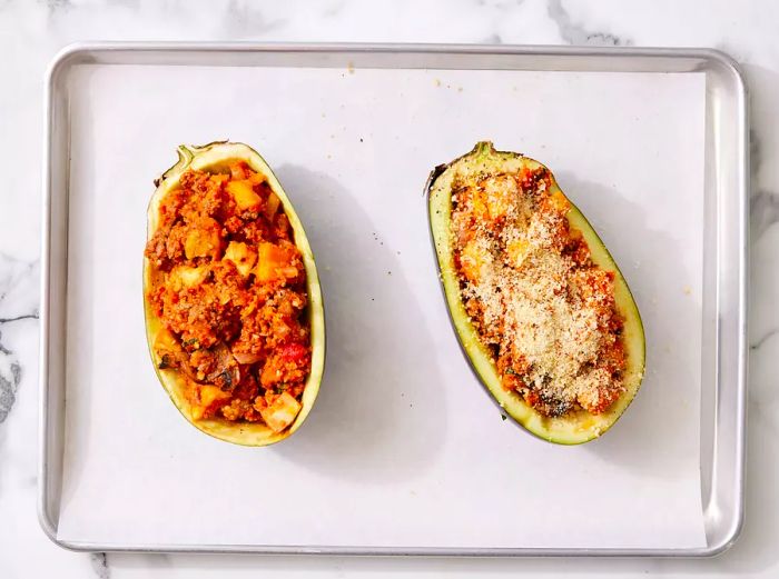 Eggplant halves on a parchment-lined baking sheet, filled with the sausage mixture and topped with panko and Parmesan cheese.