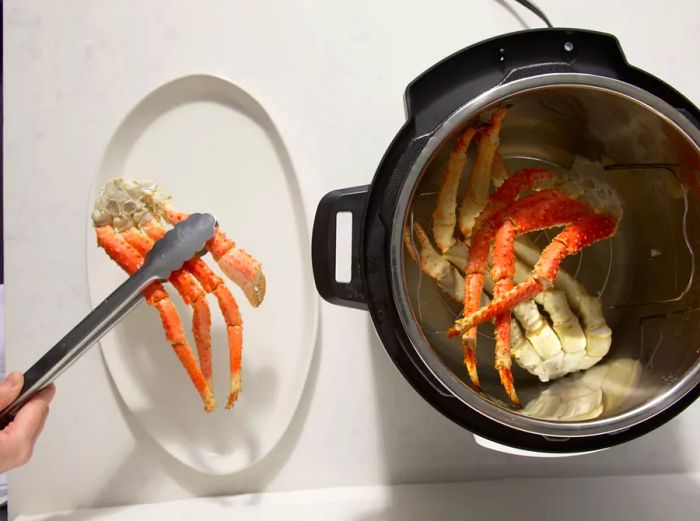 Overhead view of cooked crab legs being lifted from the pressure cooker and placed on a serving tray.