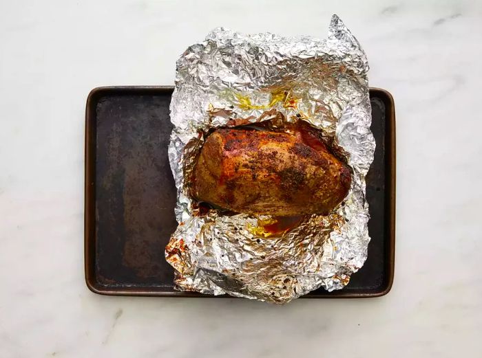 A fully cooked beef roast resting on tinfoil on a baking sheet.