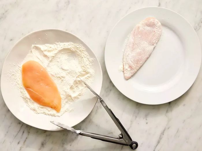 Top-down view of chicken being coated in flour on two plates