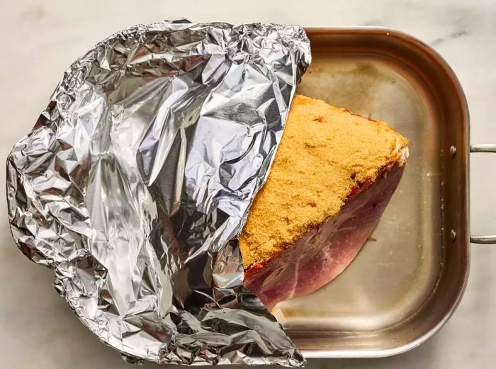 Ham in the roasting pan, with half of it covered by aluminum foil