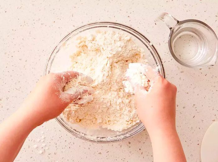 Two hands incorporating butter into a bowl of flour mixture.