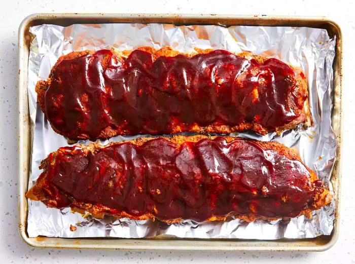 Ribs, coated with barbecue sauce, arranged on a baking sheet lined with foil.