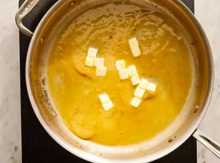 Overhead view of lemon sauce cooking in a pan, with butter cubes being stirred in