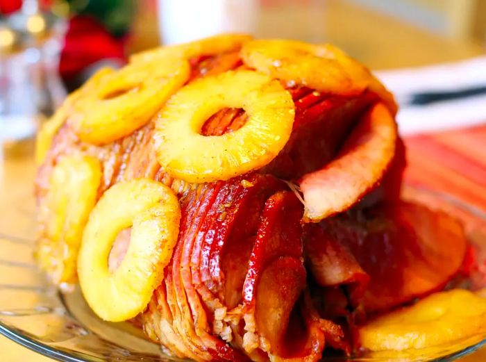 Close-up of a beautifully spiral-sliced honey-glazed ham adorned with pineapple rings on a clear glass serving platter