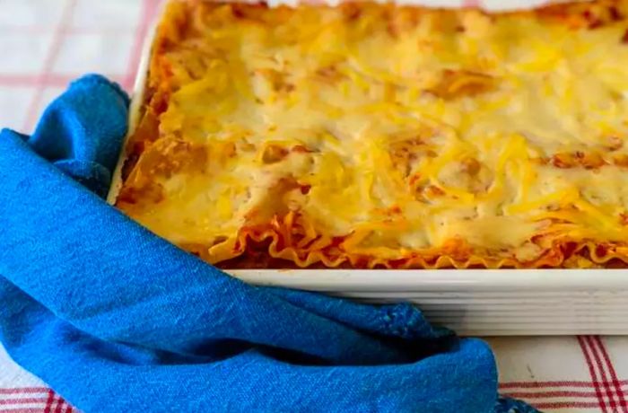 A homemade lasagna served in a white pan with a blue kitchen towel on the side.