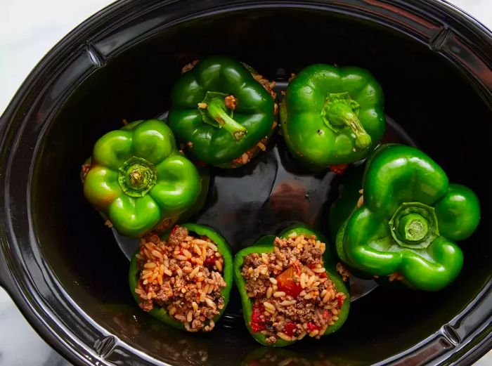 Top-down view of a slow cooker filled with stuffed green peppers, ready to be cooked.