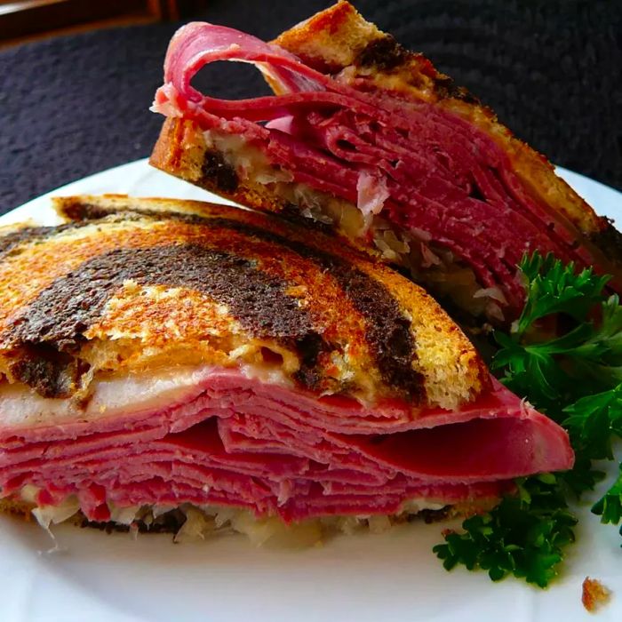 A close-up view of a grilled and sliced Reuben sandwich showcasing layers of pastrami, sauerkraut, and Swiss cheese.